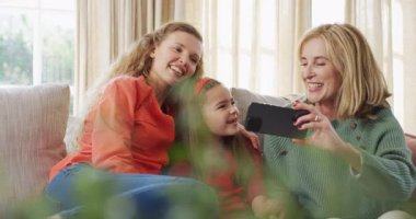 Video of happy caucasian mother and grandmother taking selfie with granddaughter on couch. Family, domestic life and togetherness concept digitally generated video.