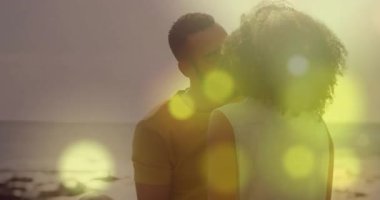 Kayalık plajda gün batımını gösteren bir yaşam tarzı. Öpüşmek için eğilen altın bokeh çifti. Romantizm, sükunet, samimiyet, siluet, manzara, sıcaklık, bağlantı