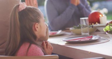 Video of happy caucasian daughter saying grace at table before family meal. Family, domestic life and togetherness concept digitally generated video.