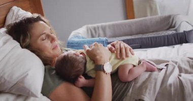 Kafkasyalı mutlu bir annenin uyuyan yeni doğmuş bir bebekle yatakta yattığı video. annelik, ebeveyn sevgisi ve yeni doğan bebek konseptiyle ilgilenmek dijital olarak üretilmiş video.