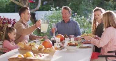 Video of happy caucasian parents, daughter and grandparents serving food and drinks at outdoor table. Family, domestic life and togetherness concept digitally generated video.
