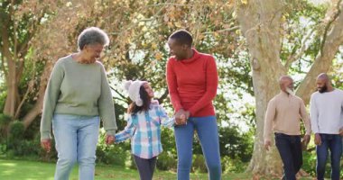 Mutlu Afrika kökenli Amerikalı anne, kız ve büyükannenin el ele tutuşup bahçede yürüdüğü bir video. Aile, aile hayatı ve birliktelik kavramı dijital olarak oluşturulmuş video.