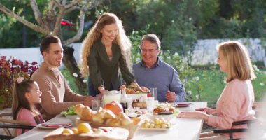Video of happy caucasian parents, daughter and grandparents serving food at table before meal. Family, domestic life and togetherness concept digitally generated video.
