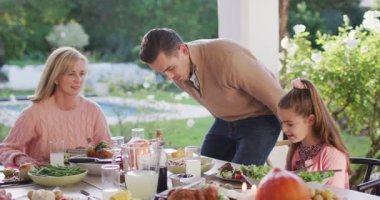Video of happy caucasian father, daughter and grandparents sitting down at outdoor dinner table. Family, domestic life and togetherness concept digitally generated video.