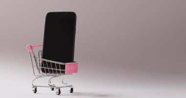 Gri arka planda alışveriş arabasında akıllı telefon. Küresel iş, çevrimiçi alışveriş, siber pazartesi, satış ve perakende konsepti dijital olarak oluşturulmuş video.