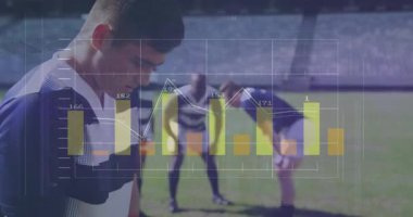 Rugby oyuncusu üst üste çizelgelerle sahada eğiliyor ölçümleri güncelliyor ve kafa gülümsemesi yükseliyor. Sporcular, spor analizleri, performans, takım çalışması, stadyum, açık hava, rekabetçi