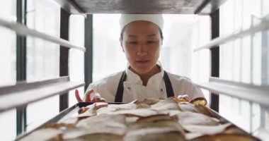 Mutlu Asyalı kadın fırıncının canlandırması yeni hazırlanmış ekmekleri kontrol ediyor. Pastanede çalışmak, bağımsız küçük işletme.