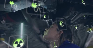 Şasi altında LED lamba kaldıran teknisyen, eklemleri tarayan ve denetim için eko simgeler üreten. Otomotiv, tanı, fütüristik, sürdürülebilirlik, teknoloji, onarım, yenilik