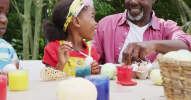 Animation of happy african american grandfather and grandchildren painting easter eggs in garden. family easter, celebration and spending quality time together outdoors.