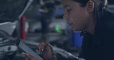 Kadın teknisyen tablet tıklatıyor ve motor bölmesi etrafında emisyon takip eden yeşil simgeler oluşturuyor. Otomotiv, teknoloji, yenilik, sürdürülebilirlik, tanı, dijital, çevresel