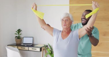 Afrika kökenli Amerikalı erkek fizyoterapistle egzersiz yapan mutlu, beyaz bir kadının videosu. Yaşlılar sağlığı ve huzurevi konsepti dijital olarak oluşturulmuş video.