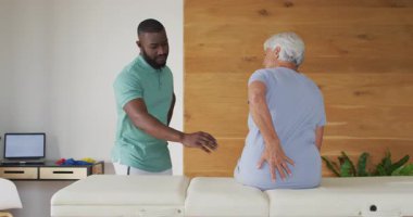 Afrika kökenli Amerikalı erkek fizyoterapistin beyaz yaşlı kadını muayene edişinin videosu. Yaşlılar sağlığı ve huzurevi konsepti dijital olarak oluşturulmuş video.