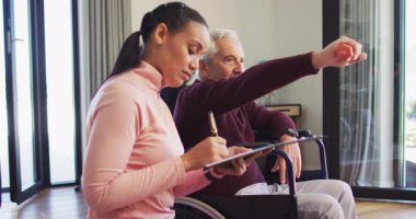 Mutlu kadın fizyoterapistin beyaz bir adamla egzersiz yapıp notlar aldığı bir video. Yaşlılar sağlığı ve huzurevi konsepti dijital olarak oluşturulmuş video.