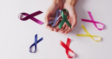 Beyaz arka planda renkli kurdeleler tutan beyaz bir kadının elleri. tıp, sağlık, kanser farkındalığı konsepti dijital olarak üretilen video.