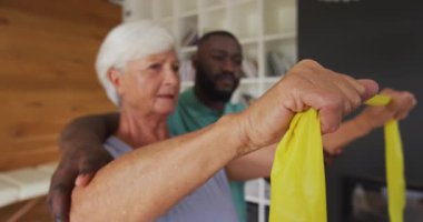 Afrika kökenli Amerikalı erkek fizyoterapistle egzersiz yapan mutlu, beyaz bir kadının videosu. Yaşlılar sağlığı ve huzurevi konsepti dijital olarak oluşturulmuş video.