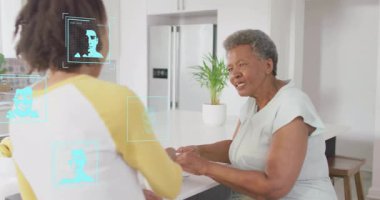 Yetişkin kız annesinin elini tezgahta tutarken aynı zamanda deniz mavisi teknolojisiyle örtüşüyor. Aile, bağlantı, teknoloji, dijital, iletişim, sıcaklık, gelecekçilik