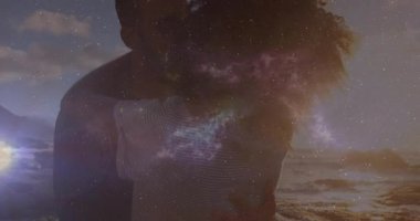 Kozmik örtüler titreyen kadın erkeği kucaklıyor ve kumlu sahil filminde aşkı paylaşıyor. Romantizm, bağlantı, gökyüzü, dinginlik, şefkat, ahenk, rüya gibi