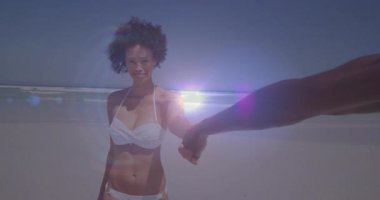 Beyaz bikinili bir kadın kumlu sahil boyunca partnerini çekerken lensler seyahat pazarlamasını arttırıyor. Romantizm, macera, rahatlama, manzara, doğal, canlı, tasasız