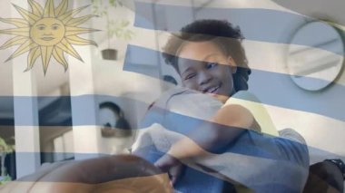 Kız kanepede babasına doğru yürüyor, aile kucaklaşmasını başlatıyor ve Uruguay bayrağı altında sallanıyor. Aile, yakınlık, yakınlık, rahatlık, sıcaklık, şefkat.