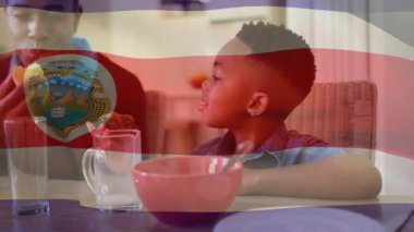 Baba oğluna kahvaltıda hamur işi sunuyor, oğul ısırıyor, anne yiyecek pazarlaması için katılıyor. Aile, kahvaltı, sıcaklık, birliktelik, doğal, samimi, samimi.