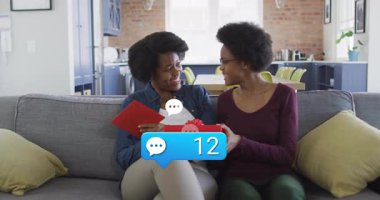 Anne ve kızının hediye kutusunu açması akıllı telefonu çalıştırması teknoloji baloncuklarının saydığını gösteriyor. Aile, kutlama, bağlantı, teknoloji, samimi, modern, neşeli