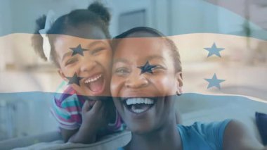 Anne ve kızı gülüyor, öpücükler savururken bayrak sosyal medya selamlaması için dalgalanırken. Aile, şefkat, kutlama, vatanseverlik, birliktelik, neşe, rahatlama