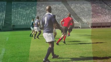 Kırmızı formalı oyuncu çim sahada ragbi topu fırlatıyor, donanma # 9 koşuyor ve kavisin altında yakalıyor. Sporcular, takım çalışması, yarışma, spor, aksiyon, adrenalin, stadyum