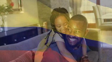 Kızınız, kanepede bayrak sallayarak eğlenmek için babanızın sırtına tırmanıyor. Aile, bağ, sevgi, rahatlık, sıcaklık, neşe, ev