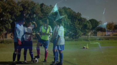 Akıllı telefon tutan oyuncu spor antrenmanlarında futbol topunun üzerine ağ örtüyor. Sporcular, işbirliği, dijital, yenilik, takım çalışması, açık hava, teknoloji