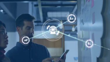 Meslektaşlar yapışkan notlar ekliyor ve iş analizleri için veri simgeleri içeren akıllı telefonları araklıyorlar. İşbirliği, takım çalışması, veri görselleştirme, dijital arayüz, beyin fırtınası, ofis ortamı, modern çalışma alanı