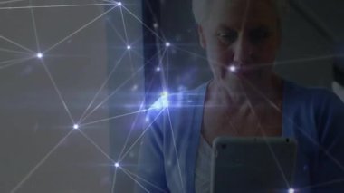 Pencerenin yanında tablet tutan yaşlı kadın dijital ağ kaplamasını başlatıyor ve sahne boyunca genişliyor. Teknoloji, bağlantı, yenilik, dijital, sinirsel, geleceksel, iletişim