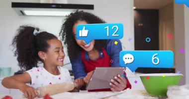 Kadın tablet tarifi okurken kız mutfakta hamuru yuvarlıyor ve sosyal konteynırların tırmandığını gösteriyor. Aile, yemek pişirme, dijital, nişan, sıcaklık, bağ, aşçılık