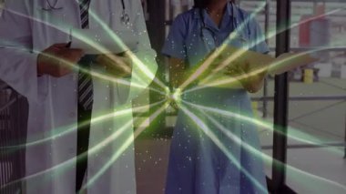 Dönen yeşil kaplama tıbbi ekibin tableti kaydırdığını ve kayıt incelemesi için dosyayı çevirdiğini gösteriyor. Sağlık, profesyonellik, işbirliği, teknoloji, tanı, klinik, yenilik