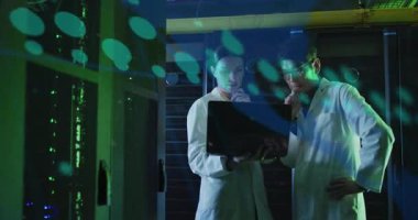 İki bilim adamı sunucu odasında yüzen yeşil veri örtüsü gösteren bir tanı yazılımı başlatıyorlar. Teknoloji, veri, analitik, yenilik, siber güvenlik, dijital, profesyonel