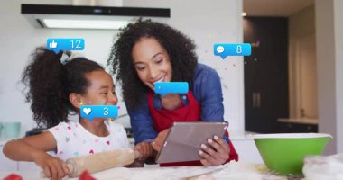 Anne tableti tıklatarak sosyal tepkileri takip ederken kız hamuru yuvarlıyor ve ikonlar yükseliyor. Aile, bağ, teknoloji, bağlılık, kutlama, yerli, yaşam tarzı