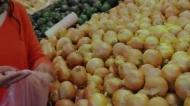 Kadın soğan kabına uzanıp yeşil kaplamayı etkinleştirirken sebze reyonunda soğan seçiyor. Pazar, sürdürülebilirlik, organik, seçim, taze, perakende, yaşam tarzı