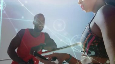 Kadın dijital grafikleri araklayıp etkinleştirirken ortağın takip cihazını kontrol etmesi ve egzersiz planlaması. Sağlık, teknoloji, açık hava, fitness, aktif giyim, bağlantı, sağlık