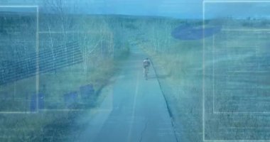 Genç bisikletçi patika boyunca pedal çeviriyor, teknoloji AR veri panellerini etkinleştiriyor ve izleme için gösterge ayarları yapıyor. Bisiklet, spor giyim, dijital arayüz, açık hava, macera, teknoloji, yenilik