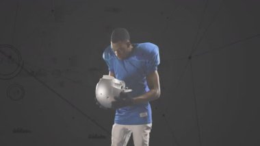Futbolcu kaskını kaldırıyor ve gri stüdyoda kayışları kayışla bağlıyor. Animasyon diyagramları yüzüyor. Sporcu, spor kıyafeti, oyun, fitness, takım çalışması, fiziksellik, motivasyon