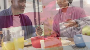 Çift pencerenin yanındaki kahvaltı masasında oturuyor, kadın cam tutuyor ve adam portakal suyu dolduruyor. Romantik, samimiyet, sabah, evcil, rahat, yaşam tarzı, beslenme