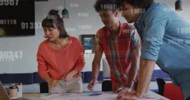 Yaratıcı ekip işaretleri ve notları düzenliyor, dizüstü bilgisayara bakıyor ve tasarım örtüşmelerini başlatıyor. İşbirliği, takım çalışması, beyin fırtınası, yenilik, yaratıcı süreç, modern ofis, planlama