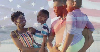 Anne kucağında oğlan, baba kucağında Amerikan bayrağı taşıyan bir kız ilanda gülüyor, aileyi birleştiriyor. Aile, okyanus, sahil, birlik, kutlama, mutluluk, açık hava