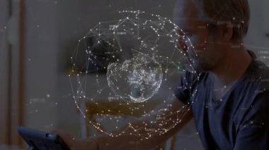 Olgun erkek evde oturup tablet kullanıyor, dönen teknoloji küresini etkinleştiriyor ve hafifçe vurarak parlıyor. Teknoloji, yenilik, dijital, bağlantı, ağ, fütürizm, akıllı aygıtlar