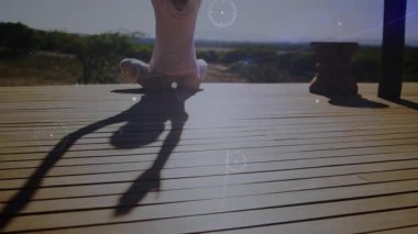 Yogi güvertede kırsal manzaranın üstünde oturuyor, kollarını yukarı doğru açıyor ve veri grafiklerini aktifleştiriyor. Açık hava, doğa, dinginlik, refah, farkındalık, manzara, minimalizm