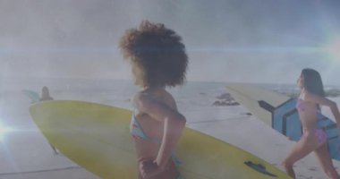 Kadınlar sörf yapmak için sörf tahtalarını dalgalara taşıyarak dalgaları duyup koşuyorlar. Rahatlama, macera, yoldaşlık, yaz, eğlence, aktivite, uyum.