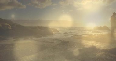 Güneş ışığı, gezmek için kıyıya adım atan siluetleri mercek alevleriyle romantizmi kutlarken gösteriyor. Romantizm, bağlantı, huzur, manzara, sükunet, ışıltı, ahenk