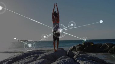 Kayalık sahilde yoga pozu veren bir kadın sağlık görselleştirmesi için parlayan düğüm ağını başlatıyor. Sağlık, açık hava, meditasyon, bağlantı, farkındalık, doğa, huzur.