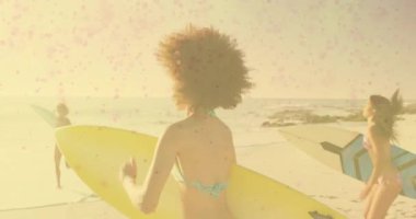 Küçük dalgalar geldiğinde sörf yapmak için renkli sörf tahtaları taşıyan üç kadın. El salla, kumsal, macera, arkadaşlık, eğlence, coşku, kıyı