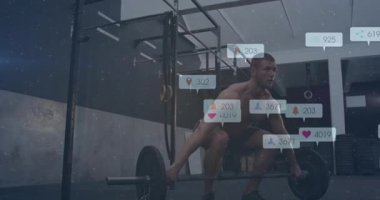 Spor salonunda halterin üzerine çömelmiş bir adam sosyal medya nişan ikonlarını çekiyor ve yükseltiyor. Kuvvet, spor, dijital, motivasyon, antrenman, atletizm