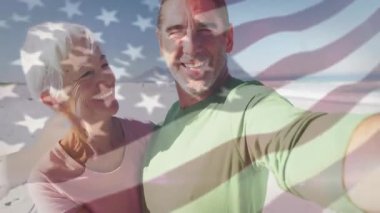 Akıllı telefonu olan adam sosyal medya selfie 'sini Amerikan bayrağıyla sahilde öpüşen çift olarak çekiyor. Romantizm, bağlantı, sevgi, manzara, yaşam tarzı, seyahat, mutluluk